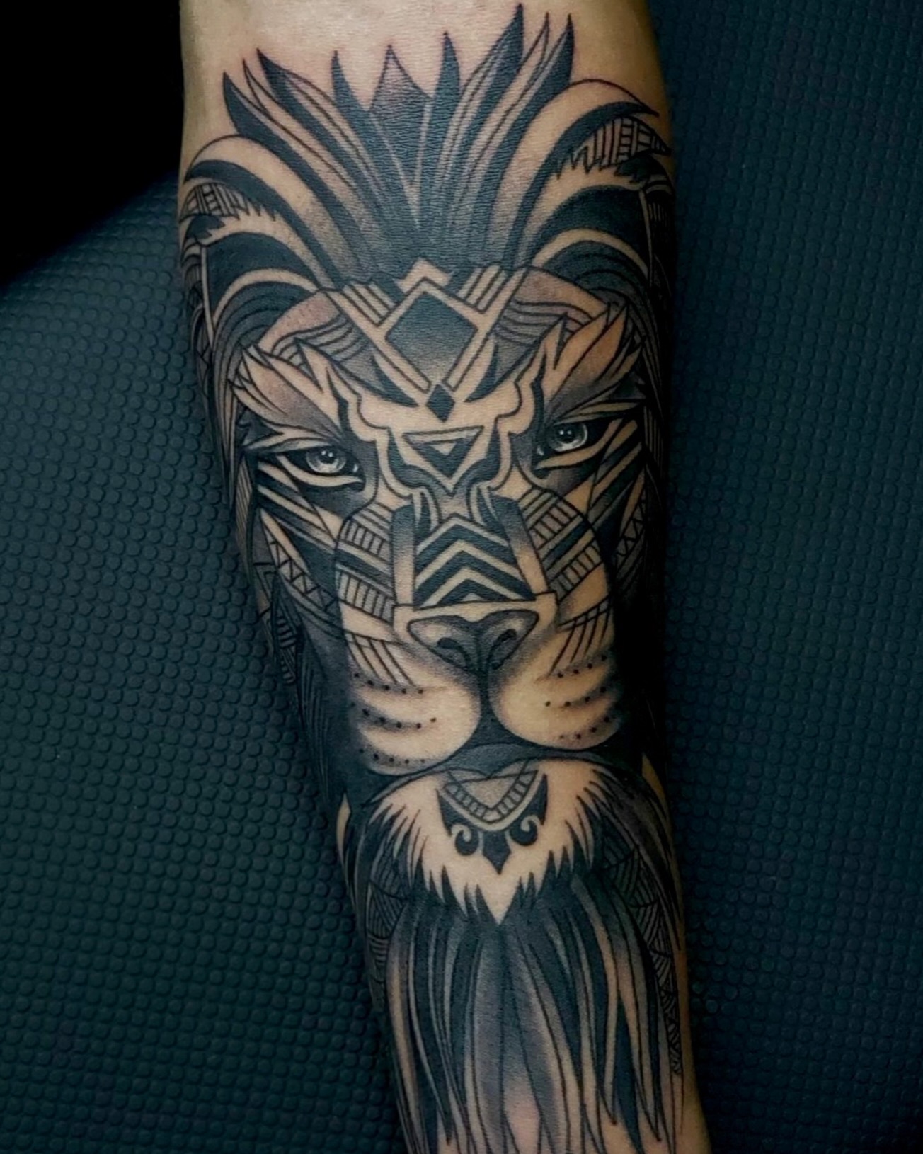 Tatuagem de leão coroado em preto e cinza no antebraço